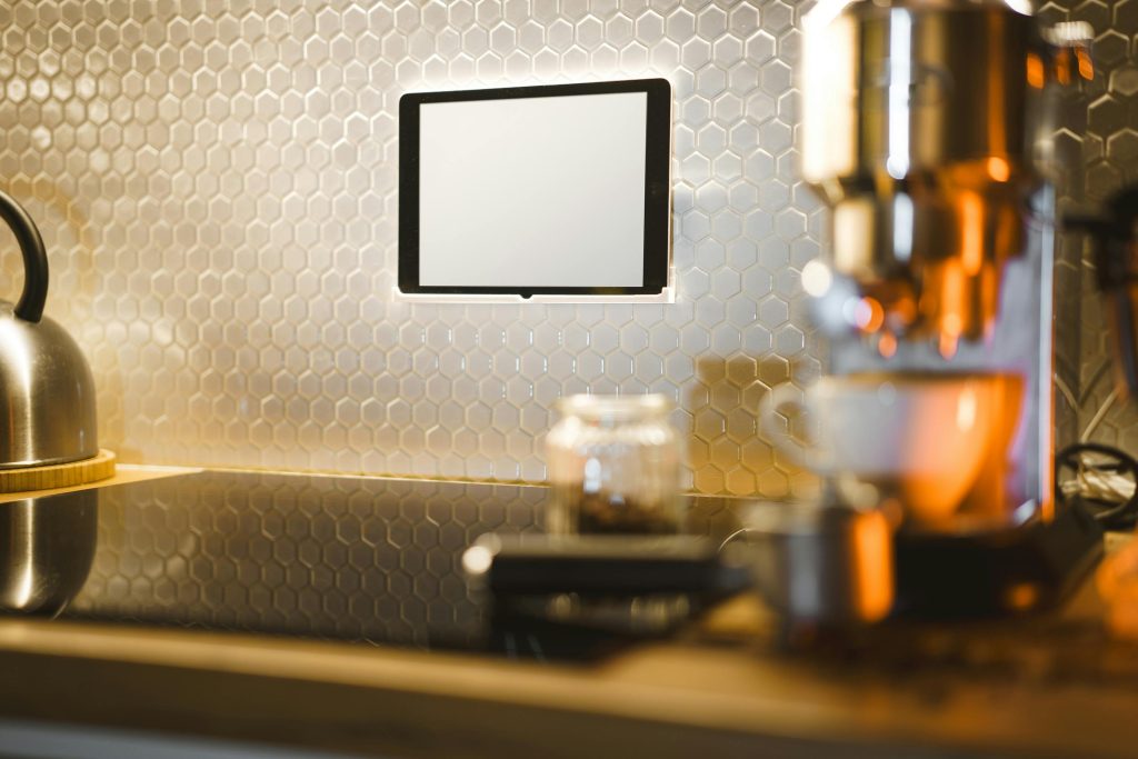 Modern kitchen counter featuring an espresso machine, kettle, and tablet on a sleek countertop.