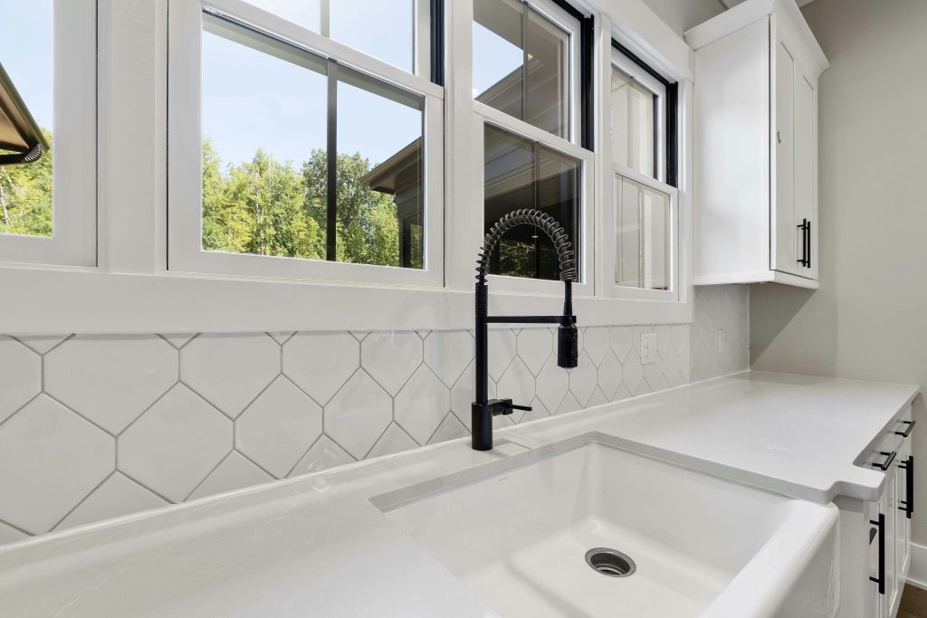 White kitchen countertop with black faucet, large windows, and modern cabinetry