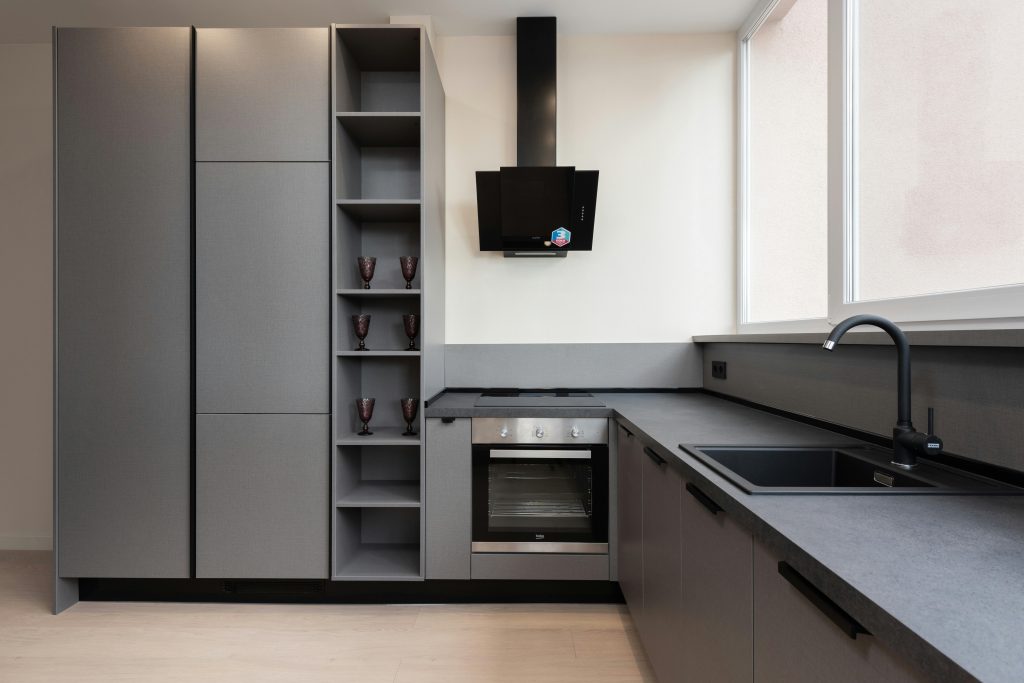 Stylish modern kitchen with gray cabinets and built-in appliances in natural light.
