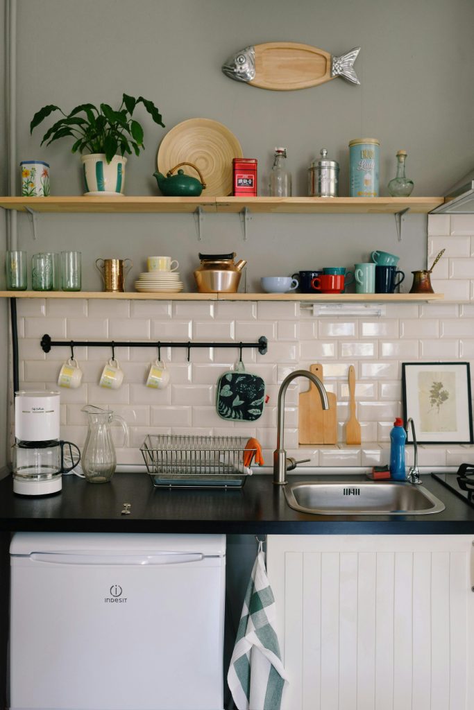 Contemporary kitchen interior with sink under wooden shelves with bowls and glasses in house