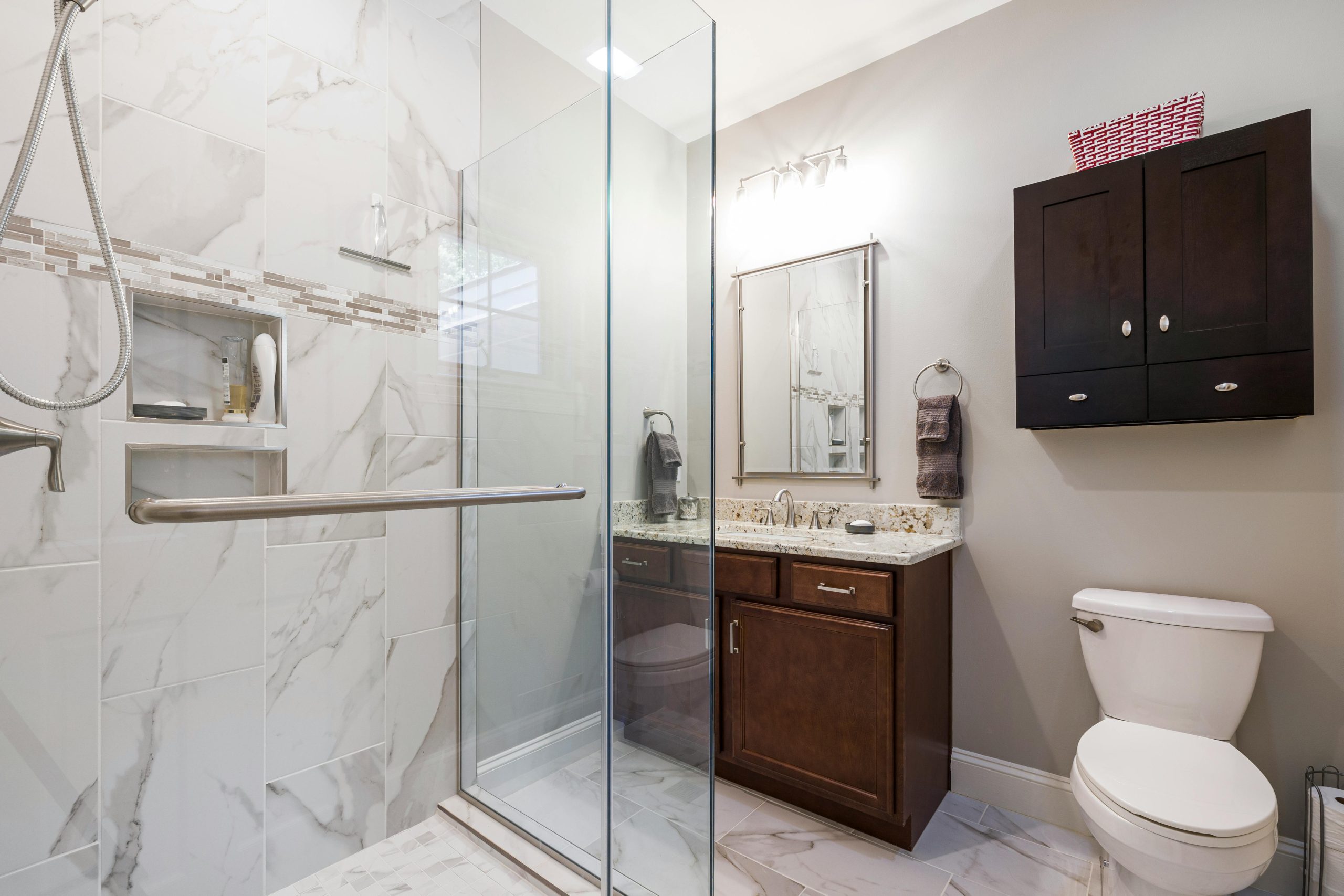 Elegant bathroom interior featuring a glass shower with marble tiles, dark wood cabinets, and modern fixtures.