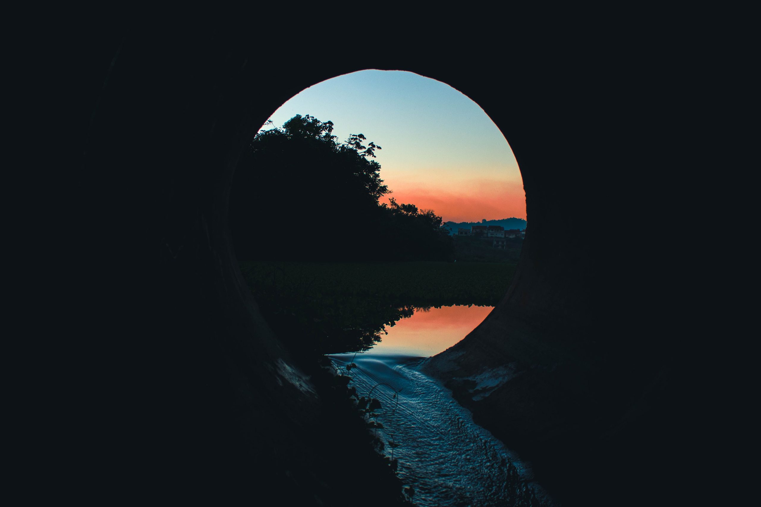 A tranquil view through a tunnel at sunset, capturing reflections on a calm body of water.